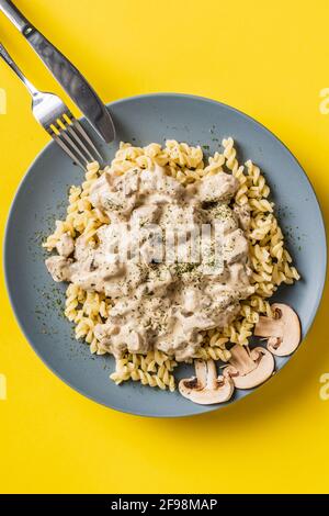 Tagliatelle con salsa cremosa ai funghi di champignon bianchi della foresta e pollo o carne di manzo - cibo fatto in casa in piatto su sfondo giallo t Foto Stock