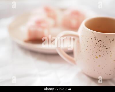 Tazza rosa e piccoli dolci rosa su sfondo bianco luminoso. Foto Stock