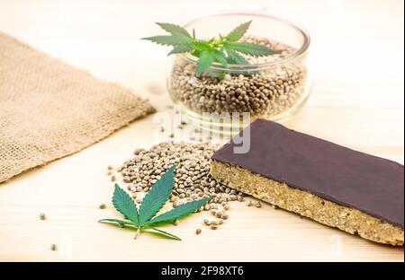 Semi di cannabis in ciotola e semi di canapa barra di cereali con cioccolato sul tavolo Foto Stock