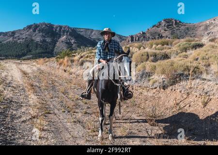 Cowboy argentino su un cavallo nero, a cavallo in Patagonia durante il giorno Foto Stock