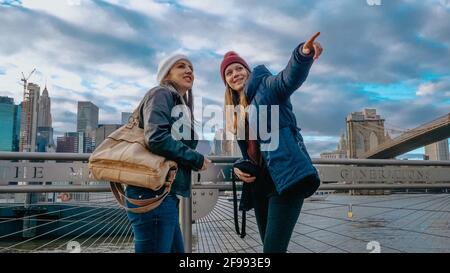 Due giovani donne a New York camminano lungo il tipico Skyline di Brooklyn Bridge - fotografia di viaggio Foto Stock