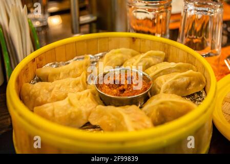 Fuoco selettivo di Momos tradizionali di Tibetian al vapore in bambù servito con chutney di pomodoro o tuffo. Foto Stock