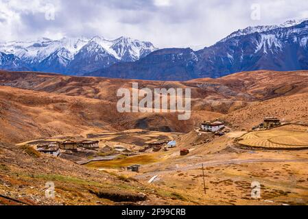 Bandiere di preghiera colorate che volano in venti con il villaggio di Komic annidato nelle montagne di Himalaya sullo sfondo nella valle di Spiti di Himachal Pradesh, India. Foto Stock