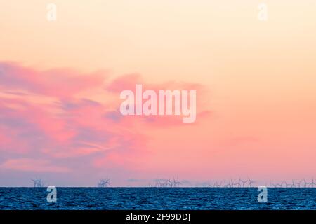 Turbine eoliche provenienti dall'offshore di Kentish Flats nel estuario del Tamigi. Orizzonte del mare basso nel telaio con le turbine appena dietro in modo da guardare mezzo tagliato. Cielo rosa all'alba con una nuvola di luce. Foto Stock