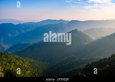 Vista della catena montuosa dell'Himalaya con silhouette visibili attraverso la colorata nebbia dal sentiero di trekking di punta di Naina. Khalia cima è ad un'altitudine di 2615m h Foto Stock