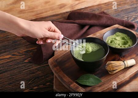 Donna che prepara il tè matcha su sfondo di legno Foto Stock