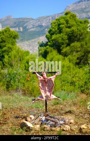 Agnello intero asado, barbecue su croce di ferro spiedo accanto al fuoco aperto in Altea la Vella, Alicante, Spagna Foto Stock