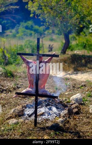 Agnello intero asado, barbecue su croce di ferro spiedo accanto al fuoco aperto in Altea la Vella, Alicante, Spagna Foto Stock