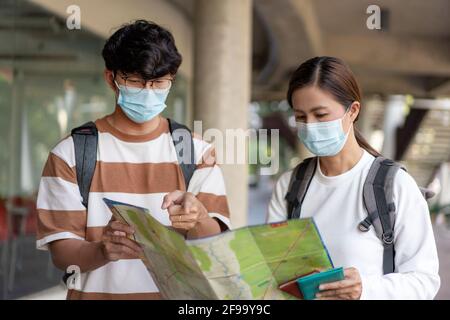 Viaggi, uomo e donna stanno leggendo carta mappa. Indossare maschera, portare zaini. Camicia spelata e occhiali. Foto Stock