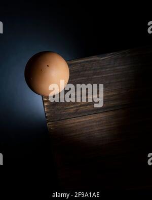 Vista dall'alto di un uovo di pollo bilanciato precariosamente sul angolo di un tavolo di legno come sta per cadere a terra Foto Stock