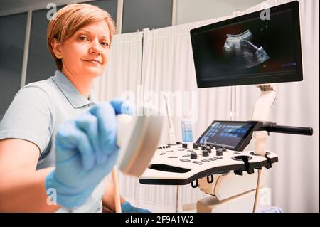 Donna in guanti sterili con trasduttore a ultrasuoni. Ecografo medico femminile che utilizza un moderno scanner a ultrasuoni in cabina ginecologica. Concetto di assistenza sanitaria e diagnostica ecografica. Foto Stock