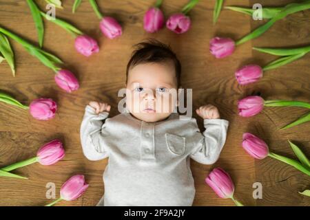 Foto del neonato bambino ragazzo o ragazza giace tra tulipani e guardando nella cornice. Grande biglietto d'auguri Foto Stock