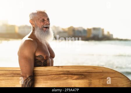 Fit Senior maschio che si diverte a navigare durante il tramonto - Allenamenti in pensione con tavole da surf sulla spiaggia Foto Stock