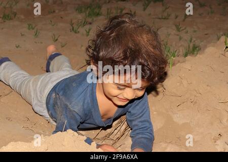 Primo piano di un bambino indiano che gioca con il suolo e posa sul terreno nel campo, concetto per l'infanzia. Foto Stock