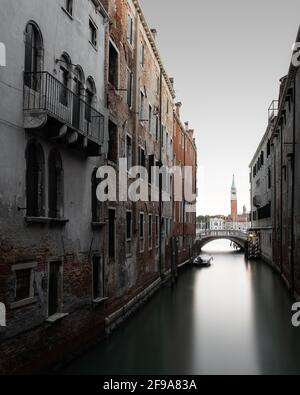 Tipico canale tra antichi edifici di Venezia. Sullo sfondo si può vedere il campanile della piccola isola di San Giorgio maggiore. Foto Stock