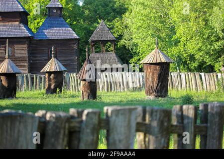 Un antico apiario rurale con antichi alveari in legno. Antichi alveari in legno nel cortile. Apicoltura. Recinzione in legno, antica chiesa in estate. PIR Foto Stock