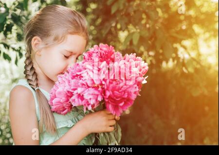 ritratto di una felice carina piccola caucasica di sette anni ragazza ragazzina, tiene in mani e l'odore e godendo di un bouquet di fiori di pony rosa in piena fioritura Foto Stock