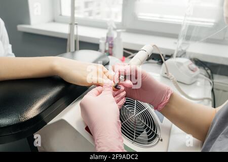 Processo di rimozione del manicure nel salone di bellezza. Il manicurista in guanti rosa rimuove la vecchia manicure. Primo piano delle mani. Foto Stock