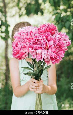 la bambina senza volto tiene in mano un bouquet di rosa fiori di peonia in piena fioritura sullo sfondo della natura Foto Stock