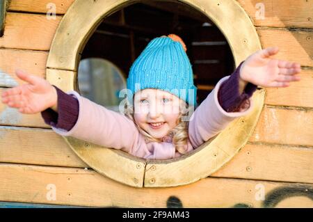 Il bambino nel parco giochi sorride con la fotocamera a braccia aperte, bambina bionda, serie di ritratti Foto Stock