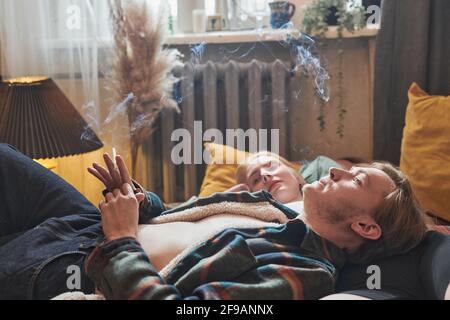 Una giovane coppia si rilassa sul letto e fuma la camera Foto Stock
