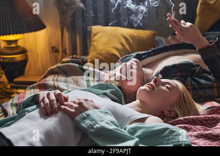 Due giovani amici che si stendano sul letto fumando una sigaretta e godendo il silenzio nella stanza Foto Stock