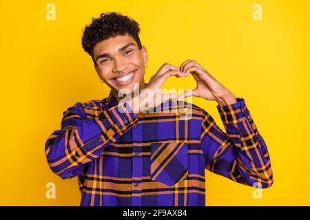 Ritratto fotografico del giovane romantico mostrando il cuore delle dita il giorno delle valentine sorridendo isolato di colore giallo brillante sfondo Foto Stock