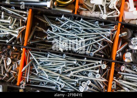 Primo piano di diverse viti, bulloni, dadi e tox separati da una scatola di plastica arancione e nera Foto Stock