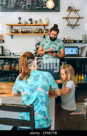 Madre che disegnano con sua figlia mentre il padre lavora nel loro caffetteria privata Foto Stock