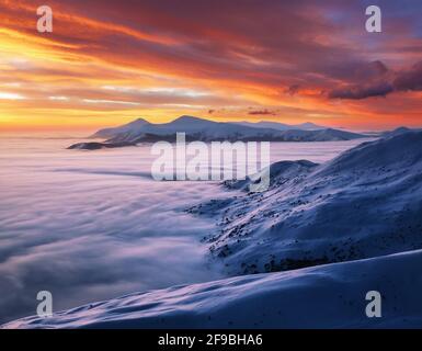 Freddo mattina invernale. Cielo incredibile con nuvola arancione. L'alba fantastica illumina la montagna, la nebbia fitta e l'orizzonte. Sfondo sfondo. Posizione Foto Stock