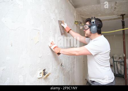 Lavoro di costruzione intonacando cemento su parete. Costruttore che indossa guanti di sicurezza, occhiali e cuffie. Foto Stock