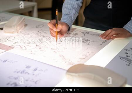 Primo piano di un'irriconoscibile designer di veicoli femminile in piedi al tavolo e. disegno di un componente dell'auto Foto Stock