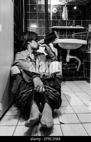 Ubriaco uomo si siede in un bagno e bere whiskey Foto Stock