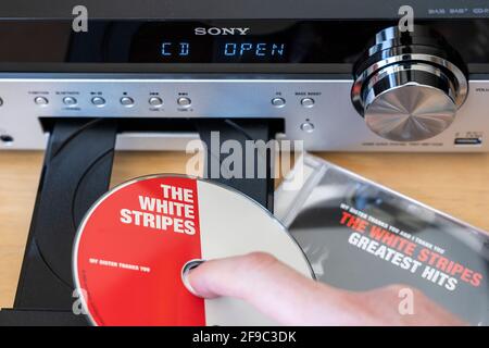 Una mano di un uomo che tiene un CD e lo mette dentro Un vassoio CD in un impianto stereo/Hi-Fi Sony con un display digitale Foto Stock