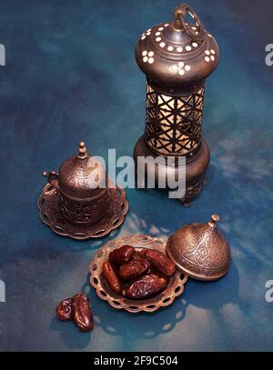 Piatto di bronzo con datteri, caffè, lanterna arabica su sfondo di legno dipinto di blu-verde scuro. Ramadan sfondo. Immagine a toni Foto Stock