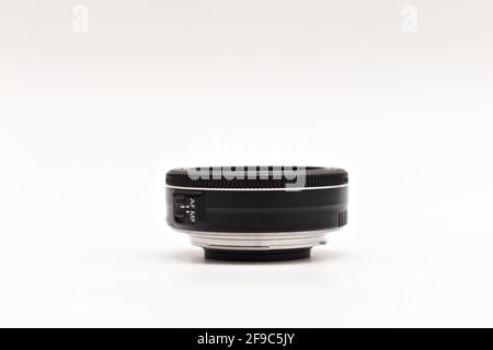 Un piccolo obiettivo nero da 24 mm senza nome per una fotocamera DSLR adagiato su uno sfondo bianco senza cappucci. Vista laterale Foto Stock