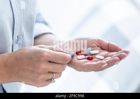 Mano femminile piena di pillole o supplementi blu, bianco e rosso. Foto Stock