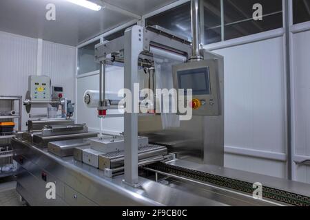 Lavorazione del confezionamento di burro e formaggio su confezionatrice sottovuoto per alimenti in fabbrica industriale alimentare. Confezionamento di burro e formaggio alimentare in pr Foto Stock