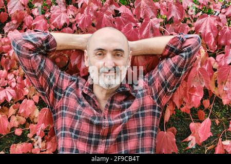 Ritratto di un uomo caucasico maturo vestito con una camicia controllata con un fondo di foglie autunnali. Foto Stock