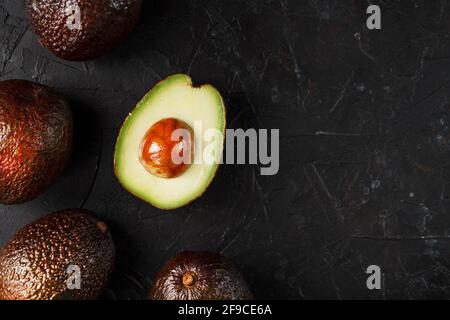 Avocado di Hass affettato maturo con osso su sfondo nero testurizzato. Vista dall'alto, spazio libero Foto Stock