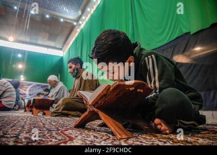 Srinagar, India. 17 Apr 2021. Un ragazzo musulmano del Kashmiri recita il libro santo islamico Corano durante la recita congregazionale del Santo Corano il 4° giorno del Ramadan in un Imam Badah a Srinagar.il mese più sacro dell'Islam, Ramadan, è un periodo di intensa preghiera, digiuno da alba a tramonto e feste notturne. Khatam al-Quran è una cerimonia normalmente tenuta dai musulmani verso la fine del Ramadan. L'osservanza segna il completamento della lettura dei 30 capitoli (Juzuk) dell'al-Quran. (Foto di Idrees Abbas/SOPA Images/Sipa USA) Credit: Sipa USA/Alamy Live News Foto Stock