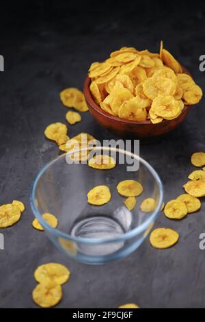 Chip di banana essiccati o cialdati di banana, disposti splendidamente in una pentola di argilla e ceramica con sfondo bianco testurizzato. Foto Stock