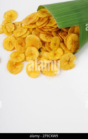 I trucioli di banana essiccati o i waffle di banana fuoriescono dal cono di foglia di banana allo sfondo bianco testurizzato. Foto Stock