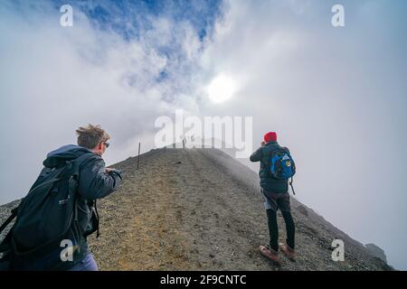 Tongariro Nuova Zelanda - Marzo 27 2021; pendii, luce e ombra sulle colline di montagne lungo la passeggiata alpina di Tongariro con scalatori che salgono in cima Foto Stock