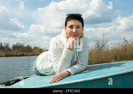 Una donna di mezza età gode dell'aria fresca all'inizio della primavera sul fiume. La donna indossa un pullover sportivo bianco. Foto Stock