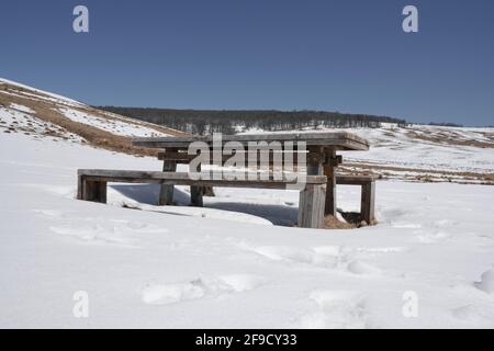 Panca e tavolo in legno nel mezzo della neve coperta highland sotto un cielo blu chiaro durante l'inverno Foto Stock