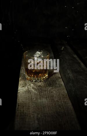 Colpo isolato di whisky con spruzzi su sfondo nero e tavolo di legno. Foto Stock