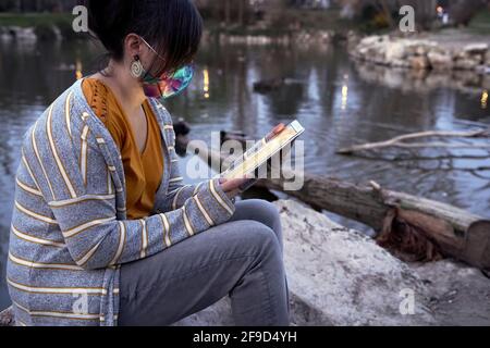 Una donna seduta sul fianco di un lago che ha un bel tempo con la tavoletta, alla notte. Concetto di calma e di svago. Foto Stock