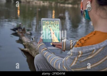 Una donna che fotografa con il suo tablet sulla riva di un lago, al tramonto. Concetto di relax e svago. Foto Stock