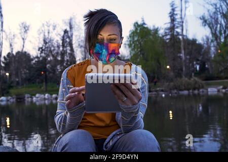 Una donna che legge sul tablet, seduto all'aperto con un lago dietro di lei, al tramonto. Concetto di calma e di svago. Foto Stock
